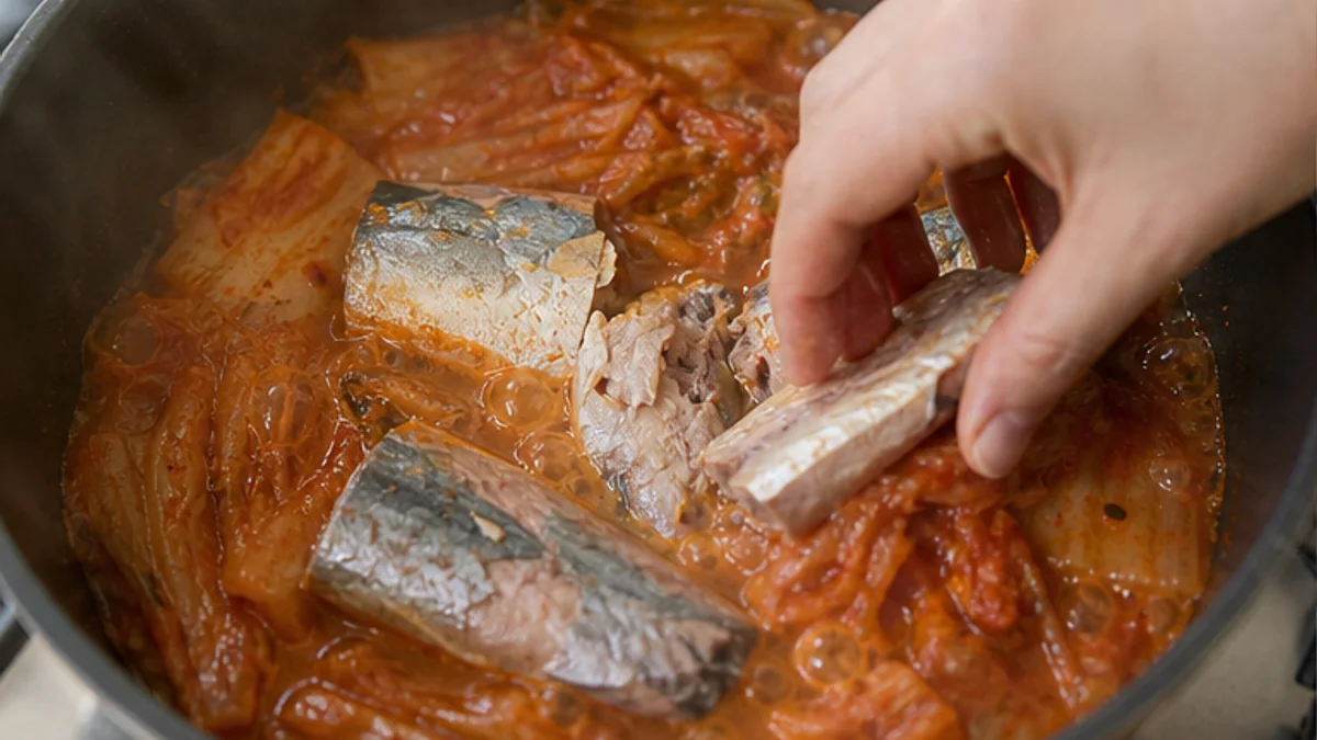 부드럽게 끓은 배추김치 위에 통조림 고등어 조각을 손으로 올리는 모습